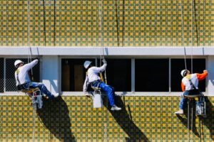 Three professional painters from Brad Stoner Painting expertly working on an exterior wall, demonstrating high-quality commercial painting services in San Diego with safety and precision.