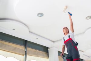 Professional painter in overalls painting a ceiling with a roller brush, representing high-quality interior painting services by Brad Stoner Painting.