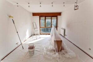 Interior painting project in progress by Brad Stoner Painting in San Diego. A freshly painted white wall, painting tools, roller, and protective coverings showcase a professional home renovation. Natural light highlights the quality craftsmanship, with a stepladder and paint buckets set up for a seamless painting transformation.